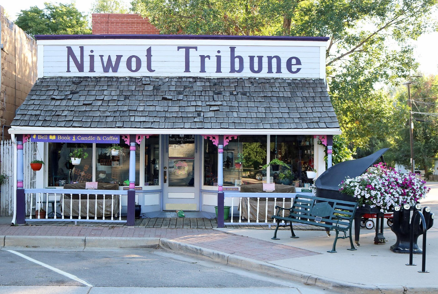 The Niwot Tribune false-front building on Second Avenue with a shingled porch roof, painted columns and a grand piano on the sidewalk